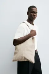 Bolso tipo shopper fabricado en piel con acabado serraje color gris oscuro. Tiene compartimento principal abierto con un bolsillo interior con cierre. Cuenta con dos asas de mano fabricadas en piel.
