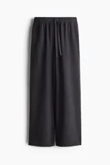 Pantalón deportivo negro de corte holgado, con cintura elástica y cordón ajustable. Confeccionado en felpa de algodón liviano con efecto lavado, bolsillos laterales y bajos sin rematar.