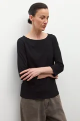 Remera negra de manga tres cuartos con escote bote y un lazo o bufanda del mismo material anudado al cuello.