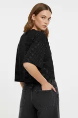 Remera blanca de manga 3/4, con cuello a la base y diseño holgado. Presenta un patrón de pequeños orificios y detalles de studs.