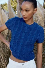 Chaqueta de punto azul con cuello redondo y manga corta. Cierre frontal con botones forrados y diseño en relieve.