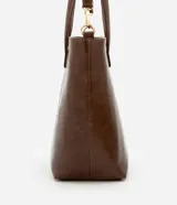 Bolso shopper grande color marrón de material sintético con doble asa, una fija y otra larga desmontable. Tiene cierre de cremallera y detalles de recortes.