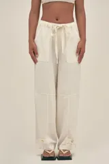 Pantalón color crema de lino y tencel, con bolsillos laterales, cintura elástica y cordón ajustable. Detalle regulable en el tobillo.