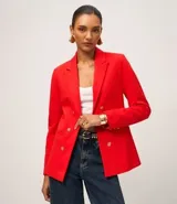 Blazer femenino de color rojo vibrante, confeccionado en tejido de punto roma. Presenta un diseño cruzado con doble botonadura de botones dorados con relieve de escudo, cuello solapa y bolsillos con tapa.