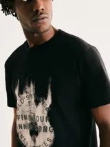 Camiseta blanca de algodón con cuello redondo y mangas cortas. Estampa rectangular con borde negro que contiene la frase "NATURAL ATMOSPHERE" en letras mayúsculas y una imagen de montañas y mar.