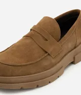 Mocasín masculino de gamuza color marrón con suela track dentada y puntera redonda. Posee el detalle clásico de antifaz sobre el empeine y costuras visibles al tono.
