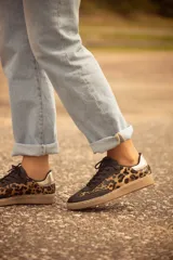 Zapatillas bajas de cuero con estampado animal print, puntera y cordones negros, contrafuerte dorado y suela color caramelo.