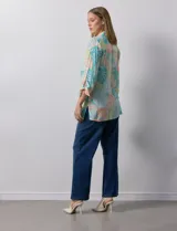 Camisa estampada con hojas en tonos celeste, naranja y verde. Tiene cuello con solapa, abertura central con botones, bolsillos aplicados en la parte delantera y mangas 3/4 con lazo.