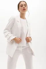 Blazer color beige confeccionado en lino, con cuello solapa, cierre frontal con un botón y mangas largas con volantes en capas.