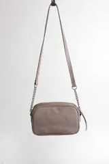 Cartera bandolera negra con diseño capitoneado en forma de V, correa de cuero y cadena plateada, cierre metálico y doble bolsillo interior.