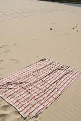 Pareo rectangular con estampado a cuadros en tonos celeste, naranja y blanco, con detalle de flecos en los bordes.