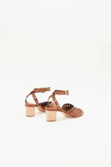 Sandalia de cuero color caramelo con taco bajo de madera. Presenta un diseño calado con bordes festoneados y perforaciones, y tira ajustable con hebilla en el tobillo.