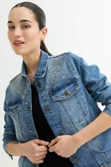 Chaqueta de jean celeste con apliques de strass en cuello y hombros, corte clásico, mangas largas y bolsillos frontales.