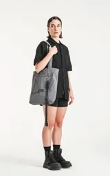 Bolso tipo tote bag color gris, confeccionado en microfibra técnica de secado rápido. Cuenta con un compartimento principal con elástico ajustable, un bolsillo interno con cierre y un bolsillo externo con velcro.