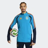 Buzo de entrenamiento Adidas Tiro España 26, color celeste con detalles en azul marino y vivos con los colores de la bandera española en los hombros. Presenta logo de Adidas en naranja y escudo de España bordado. Cuenta con cierre frontal parcial y tecnología Formotion para mayor libertad de movimiento.