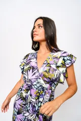 Vestido largo con estampado floral en tonos lila, verde y blanco, con escote en V, mangas cortas con volados y lazo ajustable en la cintura.