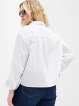 Camisa blanca de poplin, corte crop, con cuello clásico, cierre frontal con botones y mangas 3/4 con puños abotonados.