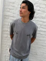 Remera gris con efecto acid wash, corte oversize y cuello redondo. Presenta un pequeño estampado negro con el texto "ON THE MOVE" y un gráfico de damero en el pecho.