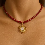 Collar corto de cuentas tubulares color rojo coral, separadas por pequeñas cuentas doradas. Dije de sol dorado con centro de circonias.