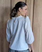Blusa blanca de algodón con cuello con volados, mangas 3/4 con bordado calado y detalle de volados en los hombros.