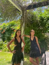 Vestido corto de lentejuelas color verde oliva, con escote en V, breteles finos cruzados en la espalda, cut-outs laterales y volado en el ruedo.