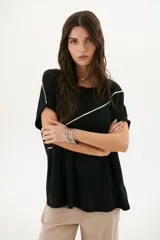 Remera negra de corte holgado con cuello redondo y mangas cortas con dobladillo. Presenta una línea diagonal blanca que cruza el frente desde el hombro hasta la cadera.