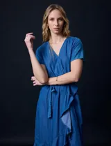Vestido de tencel azul con escote en V cruzado, cintura elastizada con lazo, manga corta con volados y falda midi con volados.