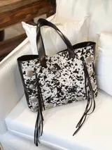 Bolso tipo tote de cuero con estampado blanco y negro, detalles de tachas plateadas y flecos de cuero negro.