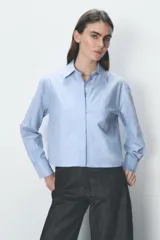 Camisa celeste de algodón con corte crop, cuello solapa, mangas largas con puños y cierre frontal con botones ocultos.
