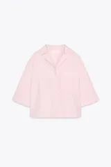 Camisa corta color rosa claro, confeccionada en algodón. Tiene cuello solapa de muescas, manga corta, bolsillo de plastrón en el pecho, bajo recto y cierre frontal con botones.