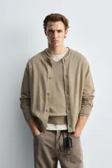 Cárdigan color beige de corte relaxed fit, tejido en hilatura con algodón y ramio. Tiene cuello redondo, manga larga, acabados en rib y cierre frontal de botonadura.