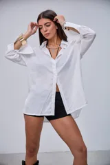 Camisa blanca de manga larga, con cuello clásico y botones frontales. Presenta puños anchos y un corte holgado.