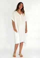 Vestido blanco de lino, corte recto, con cuello en V, mangas cortas con dobladillo y bolsillos laterales.