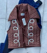 Chaleco marrón capitoneado con cuello camisero, forrado en polar y bordado con diseño de volutas en el frente. Cierre con lazos.