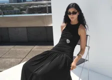 Vestido midi negro sin mangas, con cuello redondo, fruncidos laterales y diseño evasé.