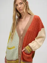 Cardigan largo color crema con detalles en color camel en el borde de los bolsillos, en el borde de los botones y en los puños. Tiene cuello en V y cierre con botones.