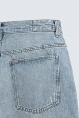 Bermuda de denim de algodón, color gris lavado, con corte relaxed fit y roturas visibles en la parte delantera de ambas piernas. Presenta cinco bolsillos y cierre frontal con cremallera y botón.