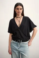 Blusa negra con escote en V cruzado, mangas cortas y corte holgado.
