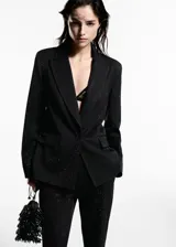 Blazer negro con pequeños apliques brillantes, cuello con solapa, cierre con un botón, dos bolsillos delanteros con solapa, forro interior y corte recto.