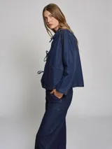Chaqueta de jean azul con cuello camisero, cierre frontal con lazos y bolsillos de parche.
