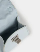 Monedero de cuerina celeste con forma de bolso pequeño, manija superior, solapa con broche de botón y mosquetón lateral con cadena plateada.