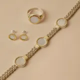 Anillo de plata 925 con baño de oro, engaste circular con piedra central de nácar blanco. El aro tiene detalles estriados en el engaste.