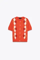 Chaqueta de punto color naranja con cuello redondo y manga corta. Presenta cierre frontal con botones y estampado de rombos en tonos blanco, naranja y marrón.