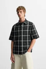 Camisa de hombre relaxed fit con estampado de cuadros blancos sobre fondo negro, cuello solapa, manga corta y cierre frontal con botones.