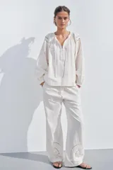 Camisa color crudo confeccionada en mezcla de algodón y lino, con cuello redondo y escote pico ajustable con lazadas. Tiene manga larga abullonada y detalle de bordados perforados a tono.