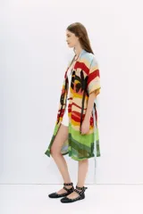 Kimono largo de lino con estampado de paisaje playero con palmeras, en tonos celeste, amarillo, rojo, verde y negro. Tiene mangas amplias, bolsillos al frente y lazo en la cintura.