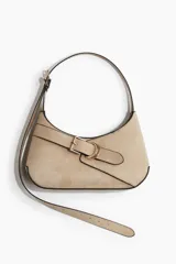 Cartera color beige con correa ajustable, cierre magnético oculto y trabilla decorativa con hebilla de metal dorada. La correa tiene un extremo extralargo para poder usar como bandolera.