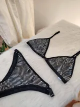 Conjunto de bikini negro con aplicaciones plateadas. El corpiño es de corte triangular con tirantes finos regulables y la bombacha es tipo colaless con laterales regulables.