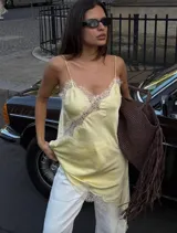 Vestido lencero corto color amarillo pálido con detalles de encaje blanco en escote, breteles y ruedo. Diseño asimétrico.