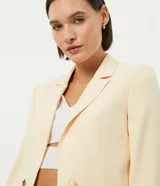 Blazer cropped color amarillo pastel, de crepé con forro de poliéster, cuello solapa, manga larga y cierre frontal con botón en forma de corazón.